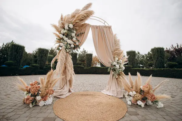 Çimlerle süslenmiş bir düğün kemeri ve taş bir verandada duran kumaş.