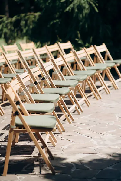 Yeşil yastıklı ahşap katlanır sandalyeler açık havada bir terasta durur.