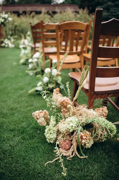 Ahşap sandalyeler açık havada çiçek aranjmanlarıyla süslenmiş yeşil bir çimenlik.
