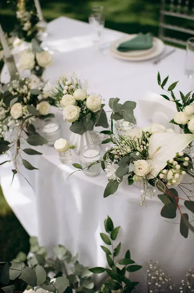 Açık hava etkinliğinde beyaz masa örtüsü üzerinde mumlar olan beyaz bir çiçek süsü.