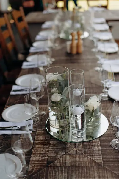 Kırsal ahşap masa seti. Zarif cam eşyalar ve şeffaf vazolarda çiçek süslemeleri.