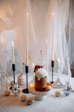 Beyaz kremalı Paskalya ekmeği ve süslenmiş bir masada mumlar ve boyanmış yumurtalarla kırmızı böğürtlen.