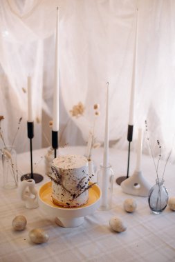 Beyaz kremalı küçük Paskalya ekmeği ve mum ve yumurtalı minimalist masa üzerinde lavanta.