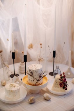 Üç küçük süslü Paskalya ekmeği beyaz kremalı, çiçekli ve şenlikli bir masada altın yumurtalı.