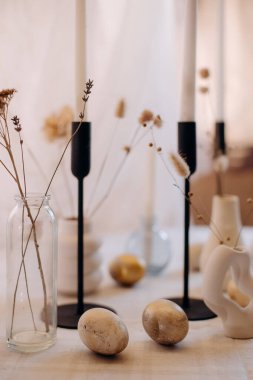 Mumlar, dekoratif yumurtalar ve yakın çekimde kurumuş çiçeklerle minimalist masa ayarı.