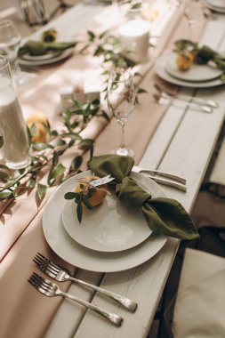 Yeşil düğümlü peçeteler ve küçük portakallar eşliğinde şık bir açık hava sofrası.