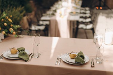 Beyaz ahşap bir masa üzerinde yeşil düğümlenmiş peçeteler ve limonlar ile şık bir açık masa.