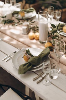 Beyaz ahşap bir masa üzerinde yeşil düğümlenmiş peçeteler ve limonlar ile şık bir açık masa.
