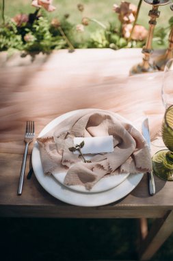 Açık havada, açık havada, açık kahverengi bir peçetenin üzerinde kanatlı bir broşla ayarlanmış şık bir düğün.