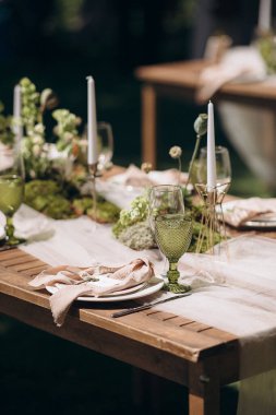 Yeşil yosun, beyaz çiçekler ve yeşil renkli bardaklarla şık bir açık hava masası.