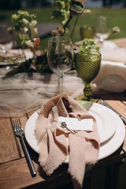 Açık yeşil keten peçeteyle bağlanmış şık bir açık hava masası.