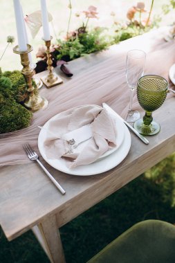 Açık yeşil keten peçeteyle bağlanmış şık bir açık hava masası.