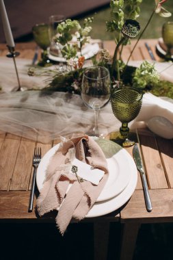 Açık yeşil keten peçeteyle bağlanmış şık bir açık hava masası.