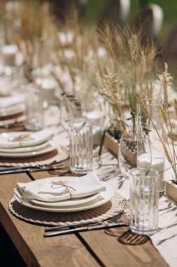 Kurumuş çiçekler, dokuma kaplar ve doğal ahşap elementlerle süslü zarif bir açık hava masası.