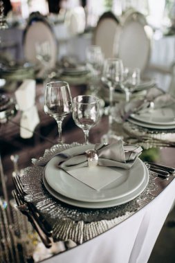 Zarif gümüş temalı düğün masası, desenli şarj plakası ve gri bağlı peçetesi var.