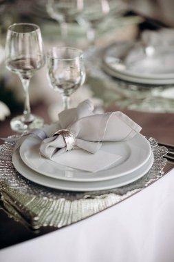 Geniş bir mekanda gümüş tabaklar, gri peçeteler ve kristal avizelerle zarif bir düğün masası.