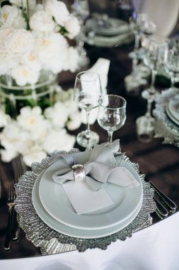 Geniş bir mekanda gümüş tabaklar, gri peçeteler ve kristal avizelerle zarif bir düğün masası.
