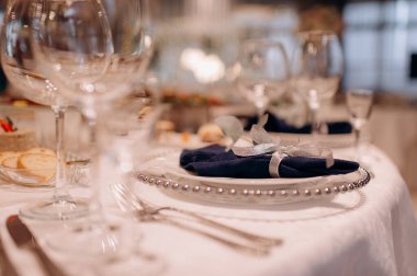 Koyu mavi bir peçeteyle bembeyaz bir masa başında gümüş bir kurdeleyle süslenmiş zarif bir masa.