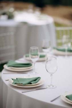 Yeşil peçeteli, beyaz tabaklı, zarif yuvarlak masa takımı ve masa numarası olan bir süs eşyası.