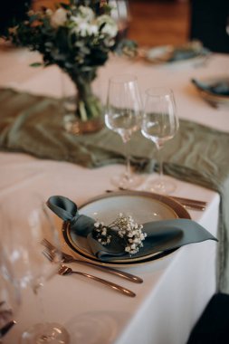 Koyu mavi bir peçete, beyaz ve altın çerçeveli tabaklar ve çiçek desenli bir masa takımı.