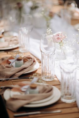 Bej bir peçete, küçük bir hediye ve ahşap bir masanın üzerinde beyaz çiçekler.