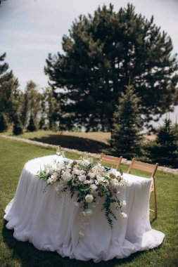 Beyaz masa örtüsü, okaliptüs çelengi ve sütun mumlarıyla şık bir açık hava düğün başkanlığı.