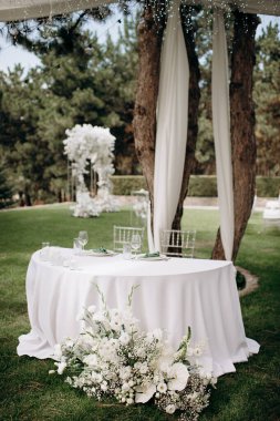 Ahşap bir masası, beyaz bir koşucusu ve narin çiçek aksanıyla şık bir açık hava düğün başkanlığı.