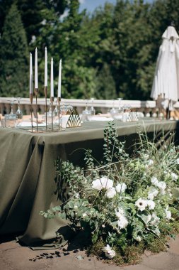 Zeytin yeşili masa örtüsü, beyaz tabaklar ve altın mum tutacağı olan zarif açık hava düğün başkanlığı.