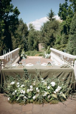 Zeytin yeşili masa örtüsü, beyaz tabaklar ve altın mum tutacağı olan zarif açık hava düğün başkanlığı.