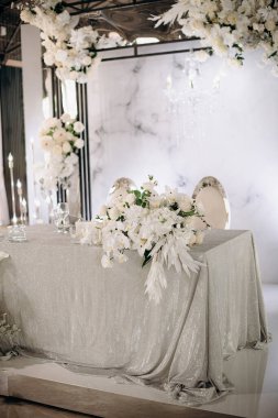 Işıldayan gümüş masa örtüsü ve yemyeşil beyaz çiçek düzenlemeleri olan şık bir iç mekan düğün başkanlığı.