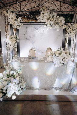 Işıldayan gümüş masa örtüsü ve yemyeşil beyaz çiçek düzenlemeleri olan şık bir iç mekan düğün başkanlığı.