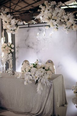Işıldayan gümüş masa örtüsü ve yemyeşil beyaz çiçek düzenlemeleri olan şık bir iç mekan düğün başkanlığı.