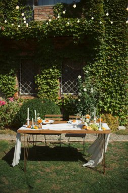 Ahşap bir masa, beyaz koşucu, turuncu çiçek aksanlı ve sicim lambalı samimi bir açık hava düğün başkanlığı.