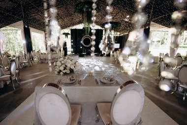 Beyaz masa örtüsü olan bir çadırda zarif bir düğün başkanı. Beyaz çiçek aranjmanları ve kristal süslemeler.
