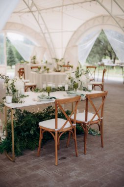Beyaz mermer bir masa ve beyaz çiçek aranjmanları olan bir çadırda zarif bir açık hava düğün başkanlığı.