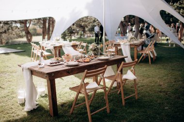 Ahşap bir masası, beyaz bir koşucusu ve yeşil çimlerde basit çiçek aranjmanları olan kırsal bir açık hava düğün başkanlığı.