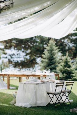 Beyaz masa örtüsü, basit beyaz çiçek aranjmanları ve yeşil çimenli açık hava düğün başkanlığı.
