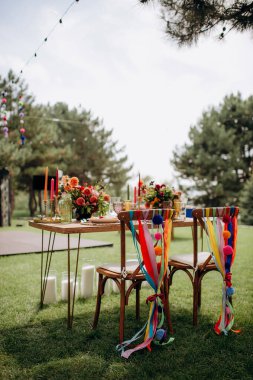 Renkli kurdeleleri, ponponları ve çiçek düzenlemeleri olan açık hava düğün başkanlığı.