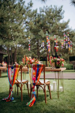 Renkli kurdeleleri, ponponları ve çiçek düzenlemeleri olan açık hava düğün başkanlığı.