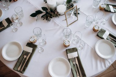 Beyaz masa örtüsü ve beyaz tabakta yeşil bir peçeteyle düğün resepsiyonunda şık bir yer.