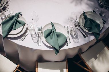 Beyaz masa örtüsü ve beyaz tabakta yeşil bir peçeteyle düğün resepsiyonunda şık bir yer.