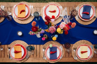 Mavi bir koşucu, renkli çiçek aranjmanları ve kırmızı biber aksanlı canlı bir düğün masasının yukarıdan çekimleri.