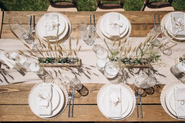 Ahşap bir masa, beyaz bir koşucu, basit çiçek aksanlı ve beyaz plakalı kırsal bir düğün masası manzarası.