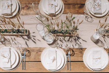 Ahşap bir masa, beyaz bir koşucu, basit çiçek aksanlı ve beyaz plakalı kırsal bir düğün masası manzarası.