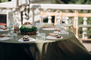 Ahşap bir masa, adaçayı yeşili bir koşucu, beyaz tabaklar ve yeşil şarap bardakları olan zarif bir açık hava düğün masası.