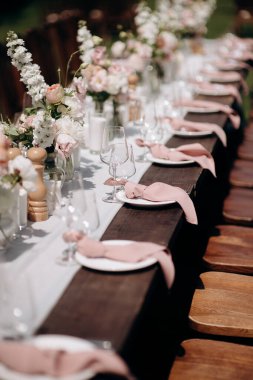Koyu ahşap bir masa, beyaz bir koşucu, pembe peçeteler ve gür çiçekli süslemeler olan şık bir açık hava düğün masası.