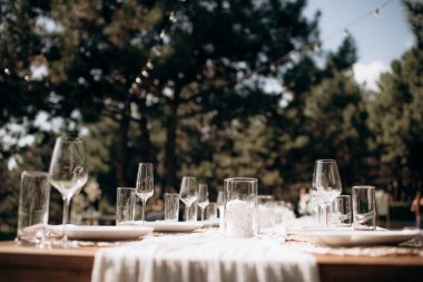 Beyaz bir masa örtüsü, bağlı beyaz peçeteler, şarap bardakları ve ahşap bir biber değirmeni olan şık bir açık hava düğün masası.