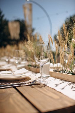 Beyaz tabaklar, dokunmuş kaplar ve basit buğday sapı süslemeleri olan zarif bir köy düğün masasının yakın çekimi.