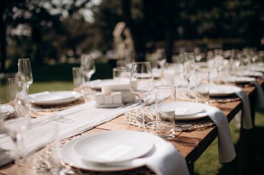 Beyaz bir masa örtüsü, bağlı beyaz peçeteler, şarap bardakları ve ahşap bir biber değirmeni olan şık bir açık hava düğün masası.