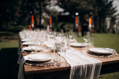 Beyaz bir masa örtüsü, bağlı beyaz peçeteler, şarap bardakları ve ahşap bir biber değirmeni olan şık bir açık hava düğün masası.